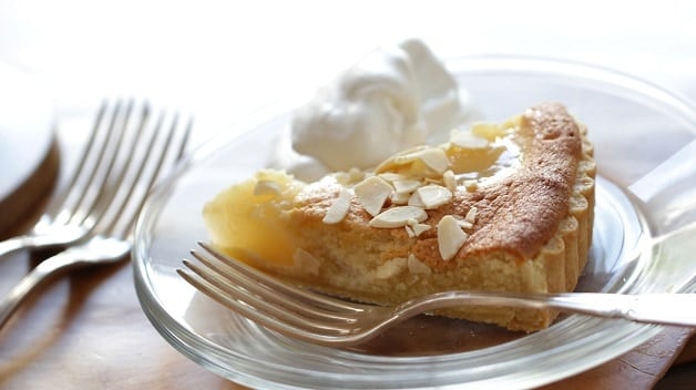 A Slice of Pear Almond Tart on a glass plate with whipped cream 