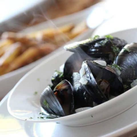 Steaming mussels garnished with parsley in a white bowl