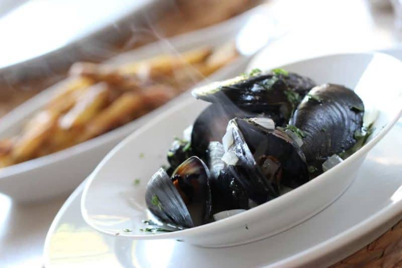 Steaming mussels garnished with parsley in a white bowl