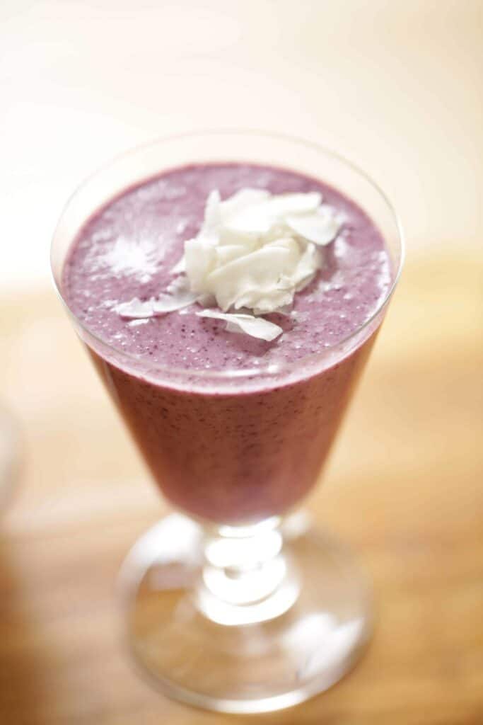 a Blueberry Coconut Smoothie in a footed glass garnished with coconut chips