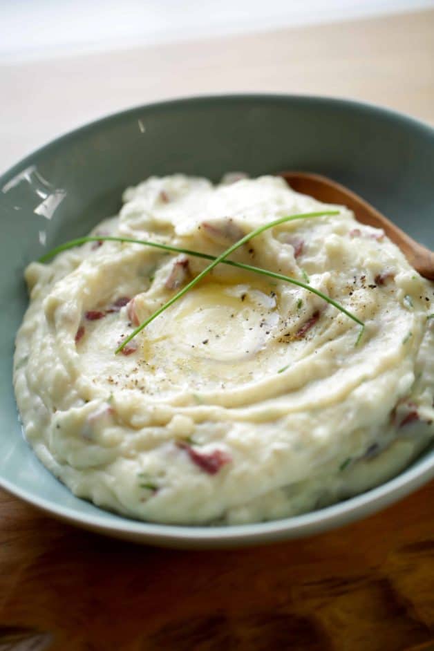  Mashed Potatoes in a blue bowl with a pool of butter, freshly cracked pepper and long chives