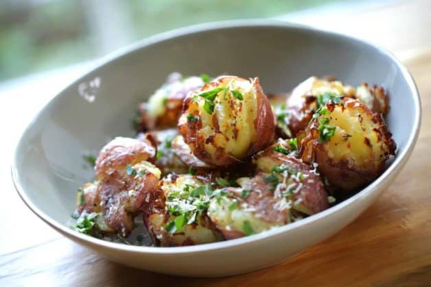 Smashed Potatoes in a gray bowl garnished with parsley and parmesean