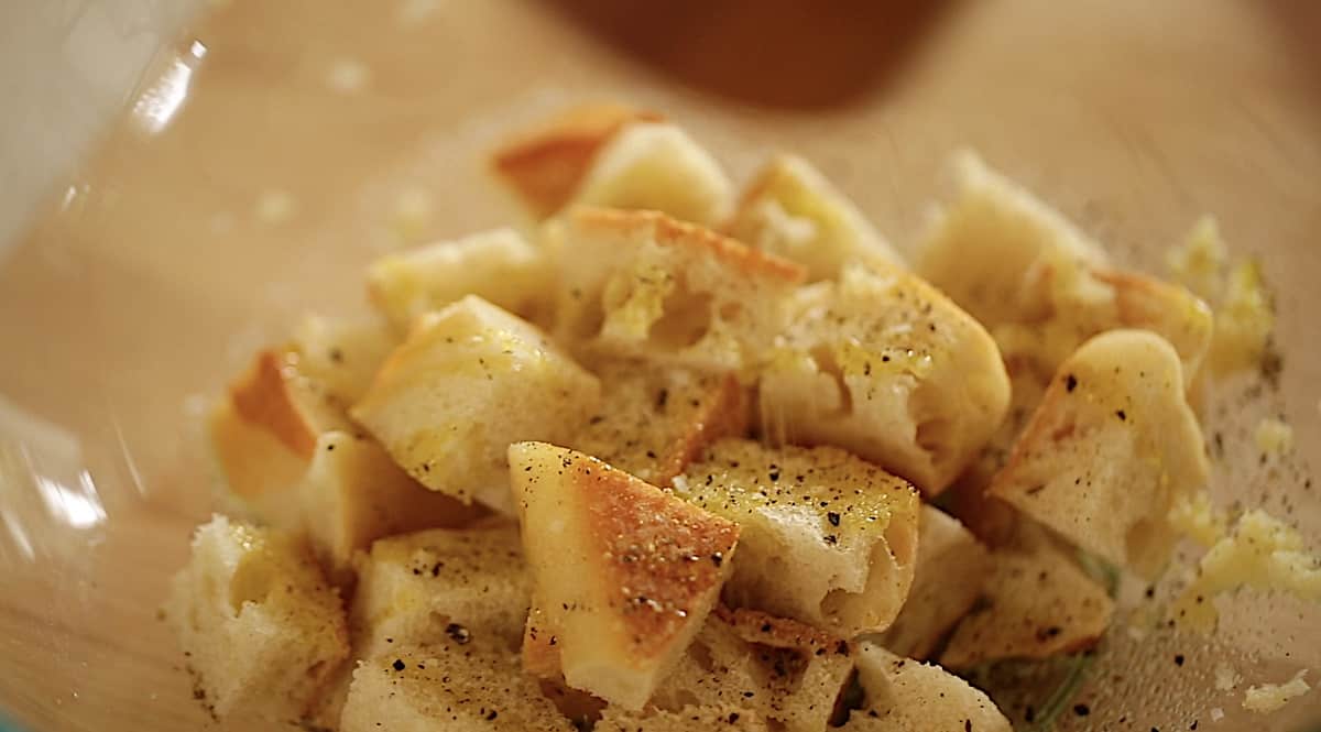 adding oil and seasonings to a bowl of cubed bread