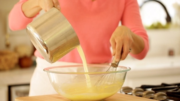 whisking cream from a pot into a bowl with egg yolks