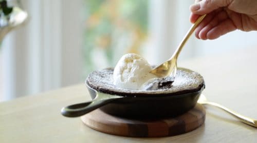 Warm Chocolate Skillet Cake with a spoon taking a bite of the scoop of vanilla ice cream on top 