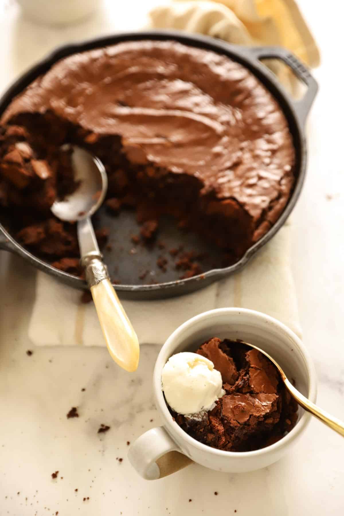 a skillet of brownie cake with a serving in a bowl with ice cream