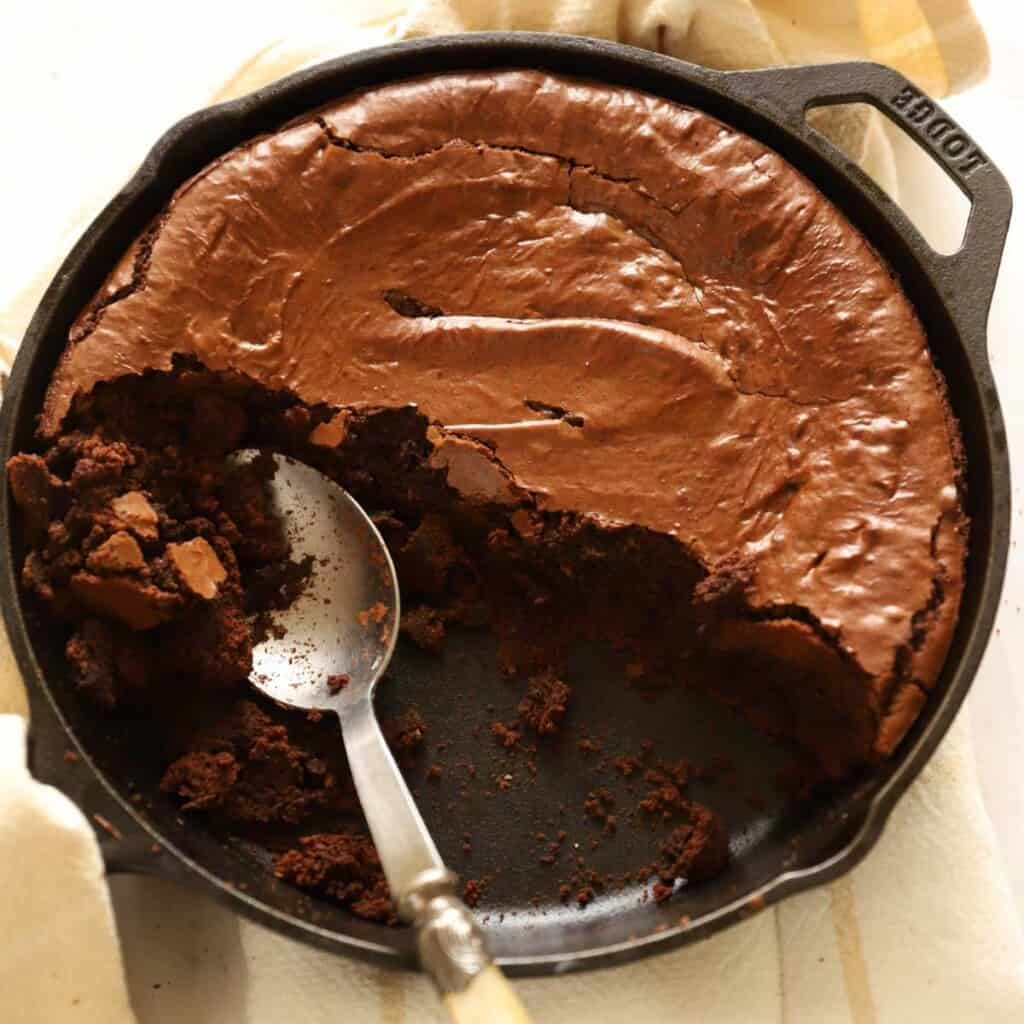 chocolate skillet cake in a cast iron pan with spoon and brownie crumbs