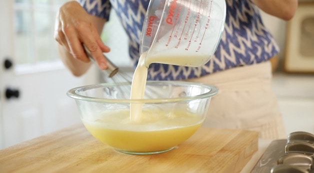 Pouring cream from a pitcher into a bowl of egg yolks