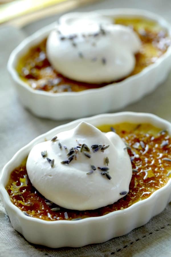 Lavender Honey Creme Brulees in a ramekin with whipped cream and lavender blossom garnishes