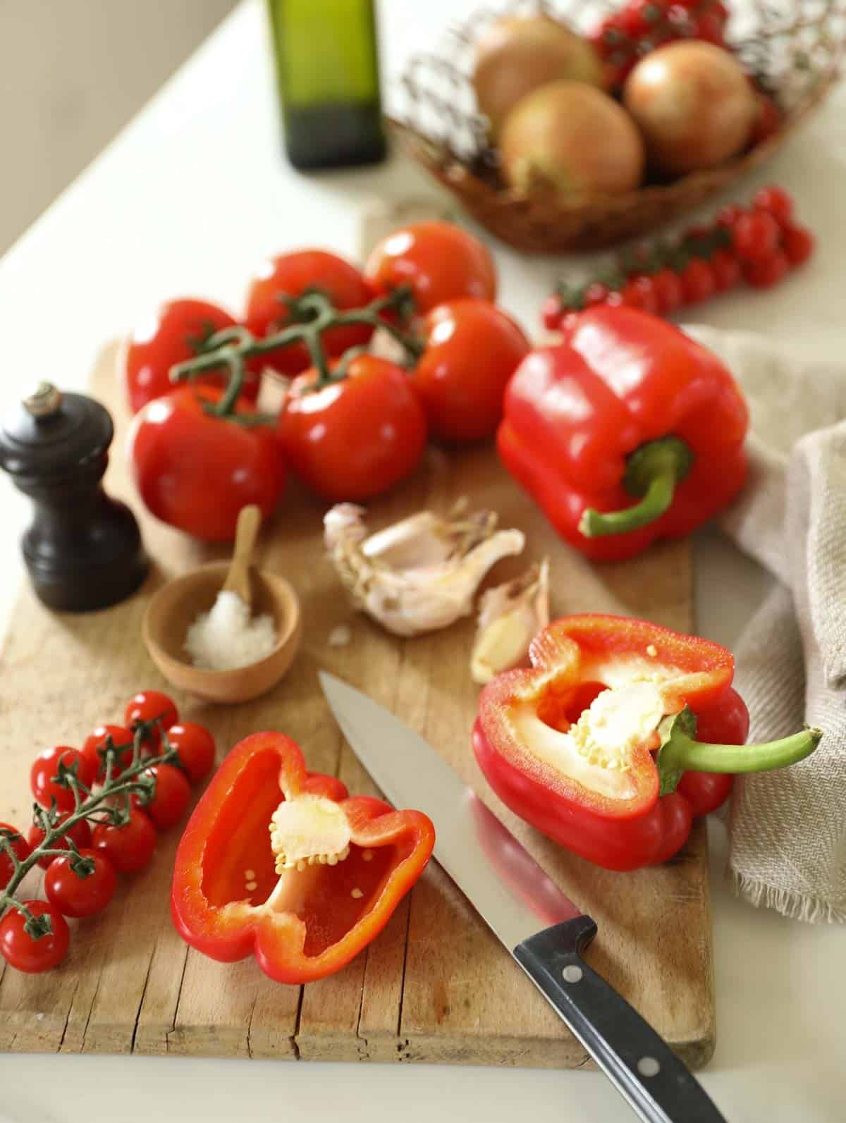 Red Bell Peppers, Tomatoes, garlic, onions and seasonings on a cutting board on a counter
