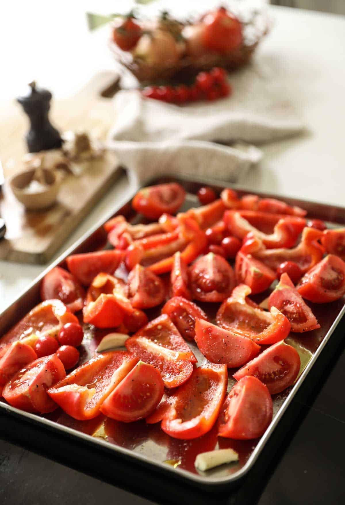 Tomatoes, peppers, and garlic on a sheet pan ready for the oven.