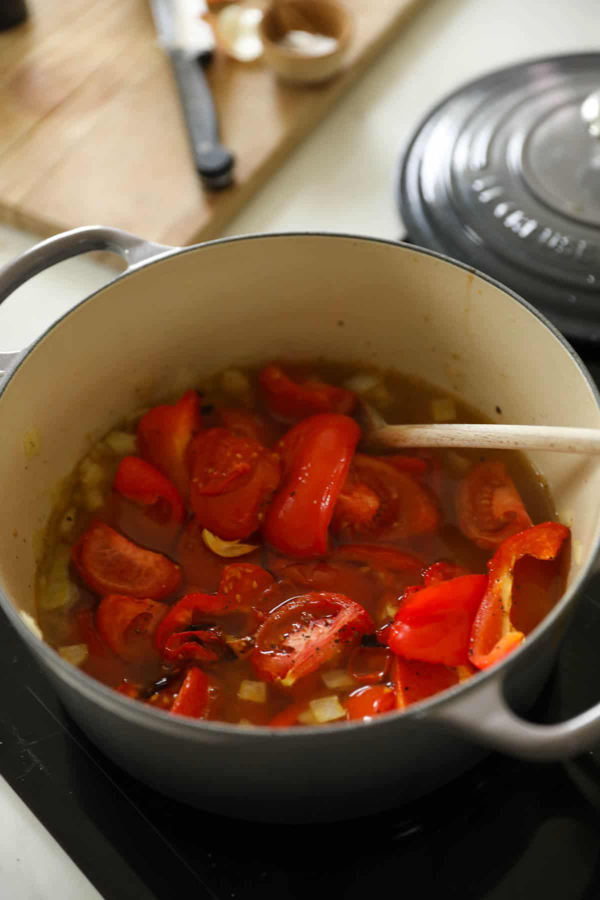 A Dutch Oven filled with tomatoes, peppers, onions and broth.