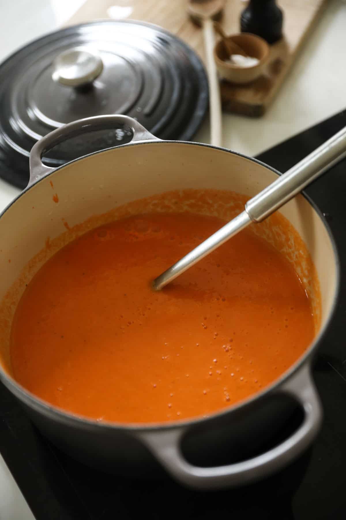 Pureed red pepper and tomato soup in a gray Dutch oven.