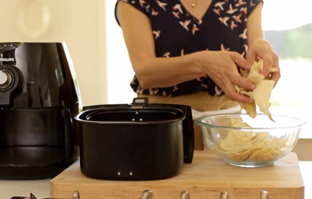 A person  transferring pita slices from a bowl to an air fryer