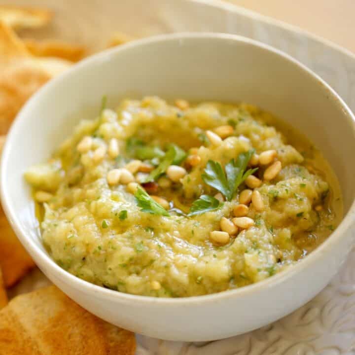 a bowl of baba ganoush garnished with pine nuts and prasley