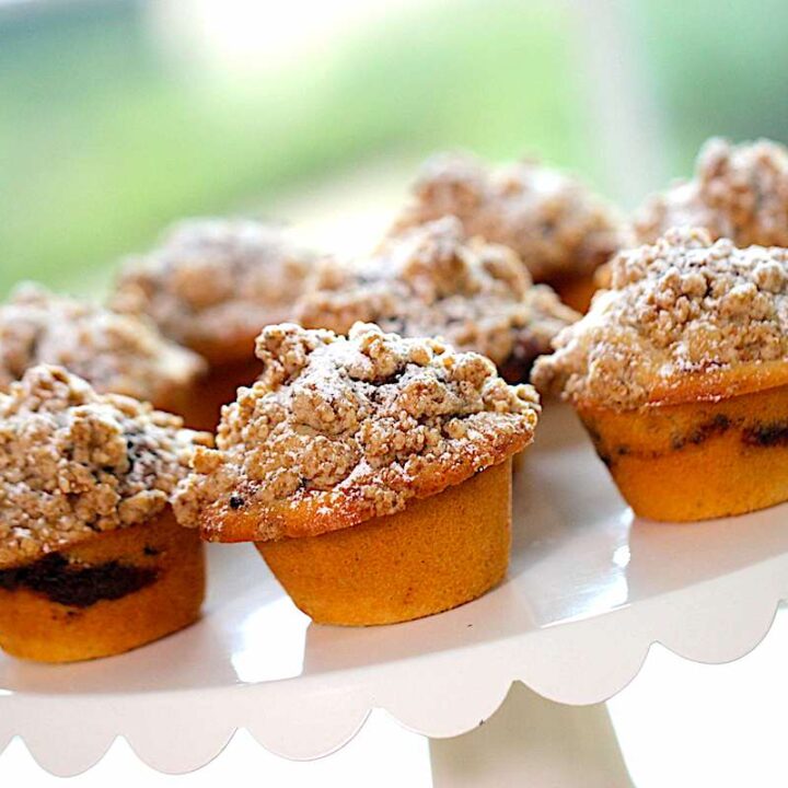 coffee cake muffins with crumb topping on a white scalloped cake stand