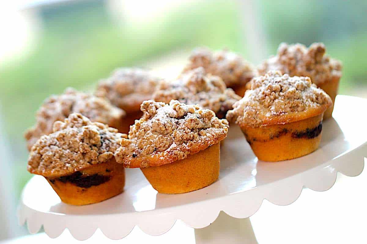 coffee cake muffins with crumb topping on a white scalloped cake stand