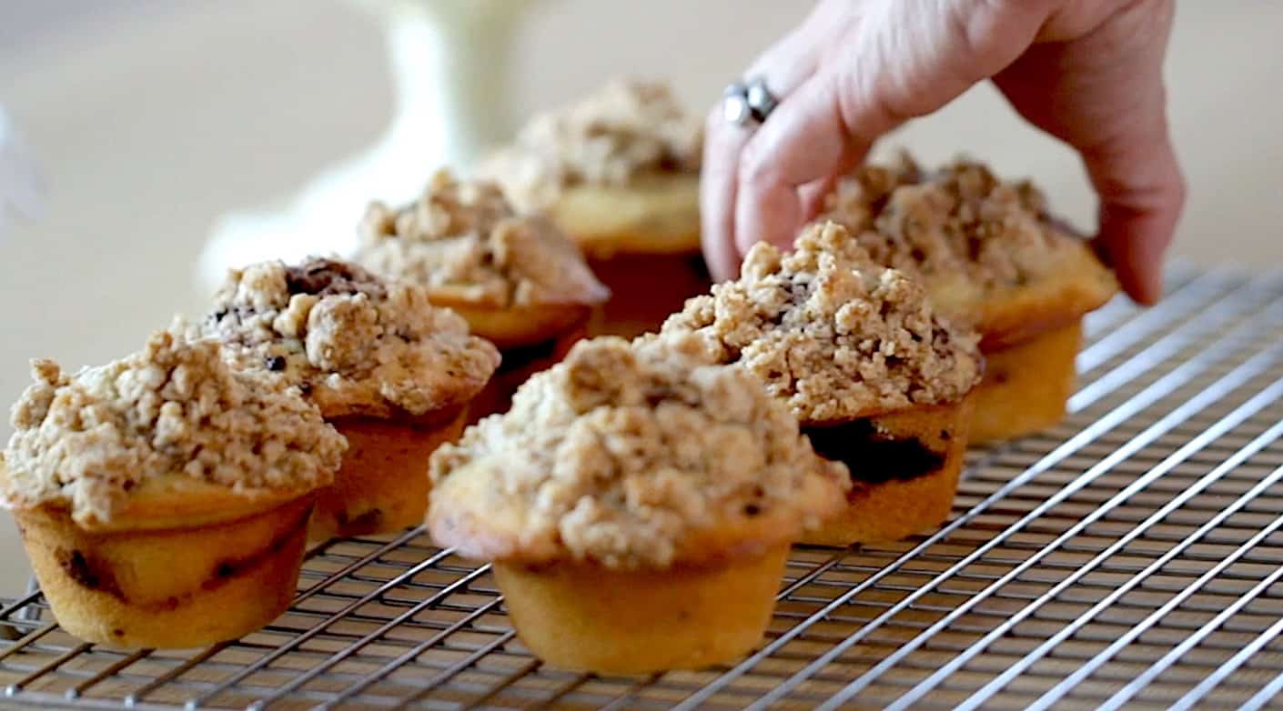 a hand placing coffee cake muffins on a cooling rack