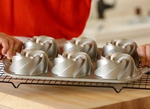 A person flipping a mini bundt cake tin on a cooling rack