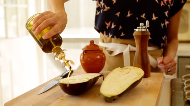 a person drizzling olive oil on eggplant cut in half