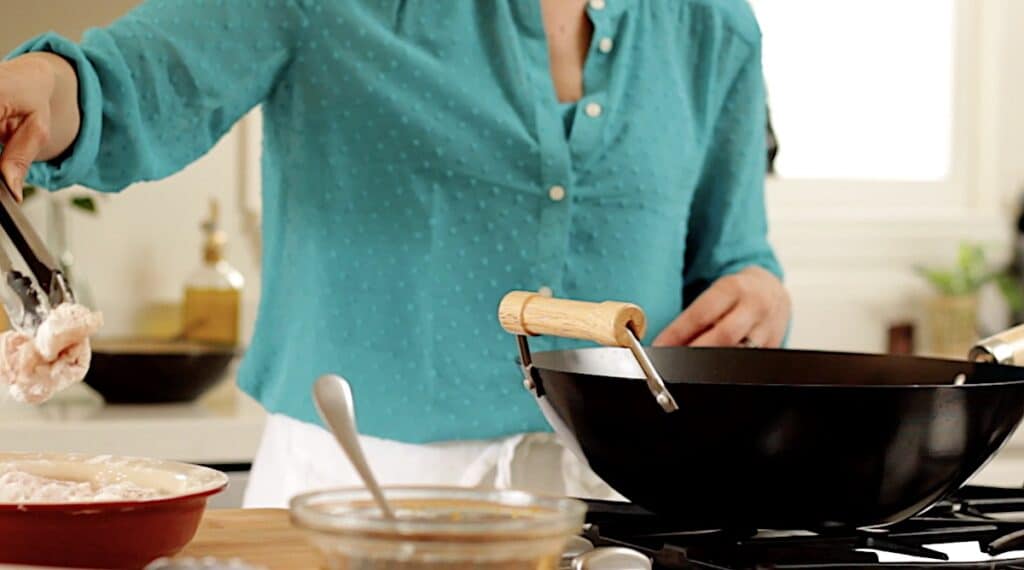 adding chicken to a wok to fry