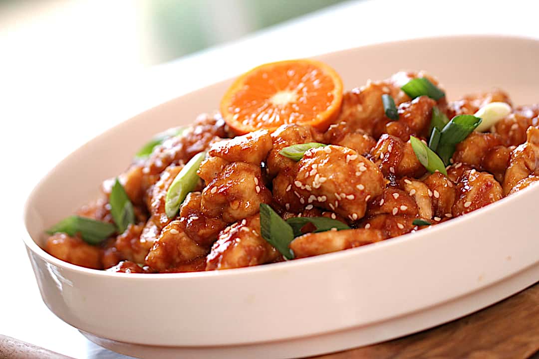a finished plate of orange chicken garnished with green onions and a slice of orange