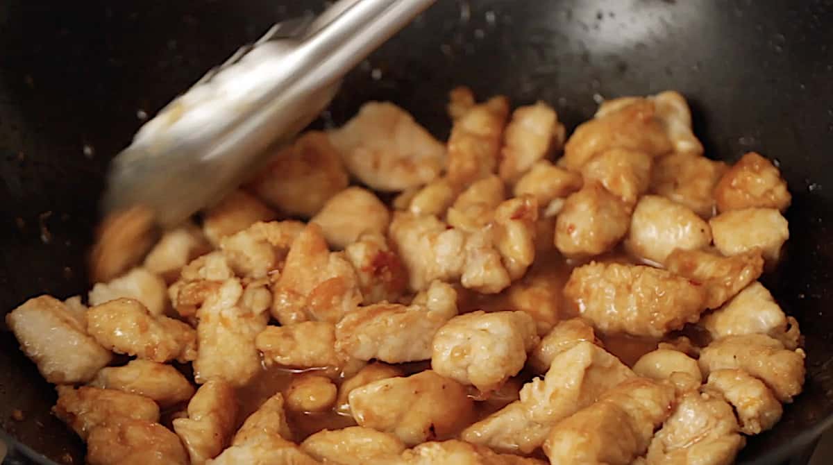 Coating fried chicken with sauce in a large wok pan