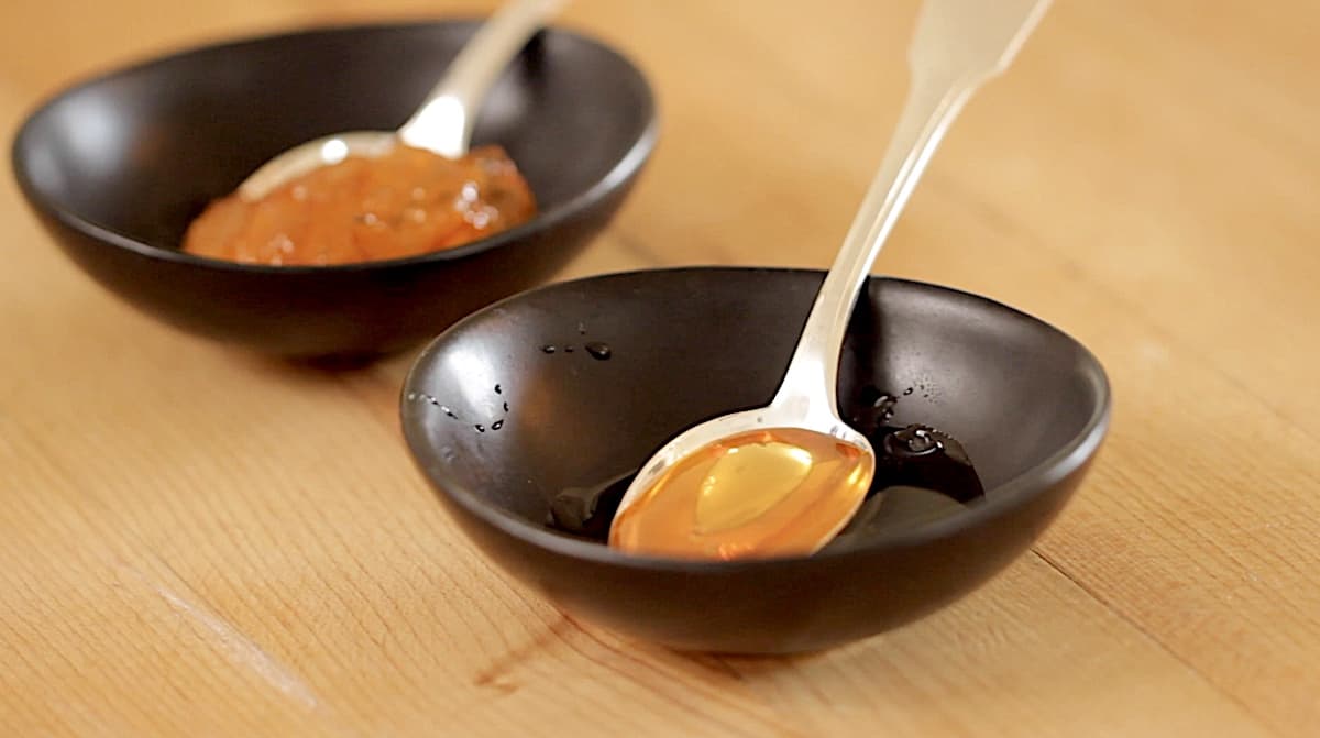 two small black dishes filled with orange marmelade and honey with spoons