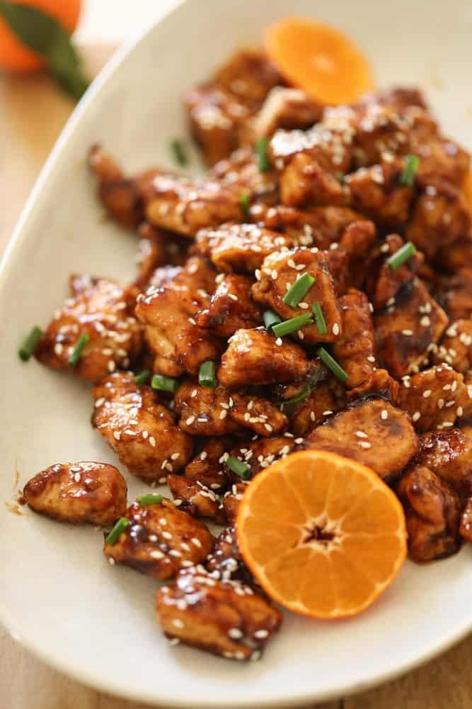 A platter of orange chicken with sesame seeds and orange slice garnishes.