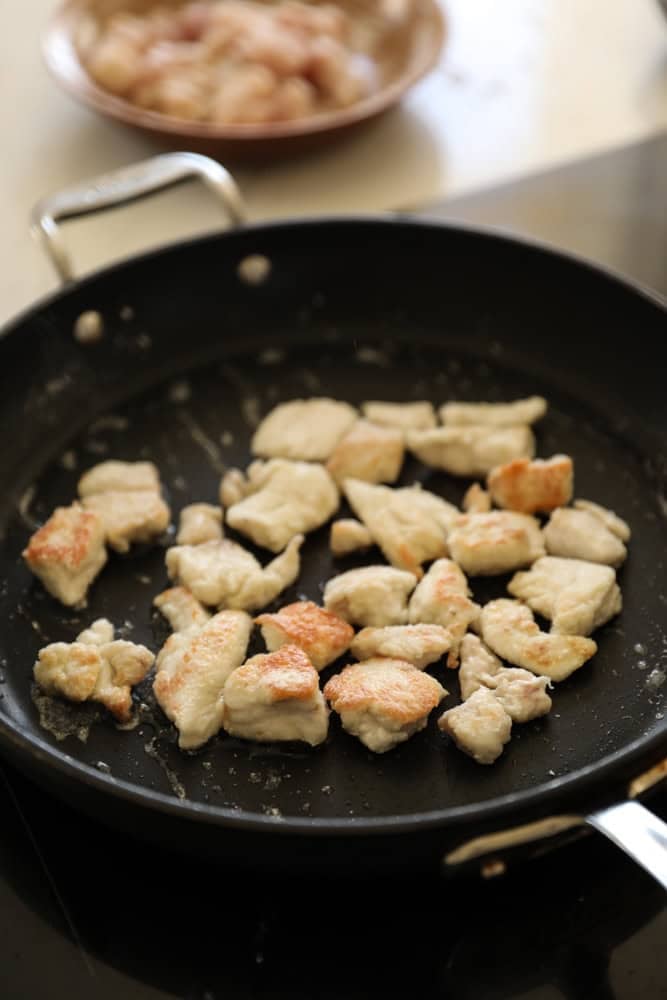 Pieces of chicken searing in a pan.