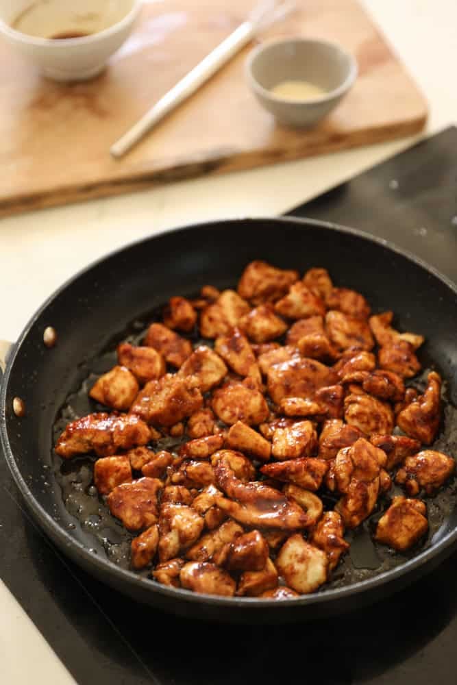 Chicken in a pan coated with orange chicken sauce.