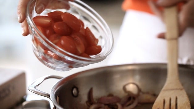 adding cherry tomatoes to a skillet of red onions