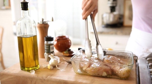 adding chicken breast to marinade dish