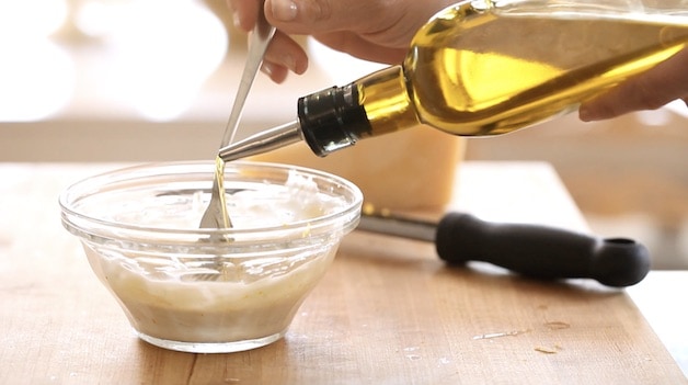 Mixing Olive oil into Caesar Salad Dressing in. a bowl