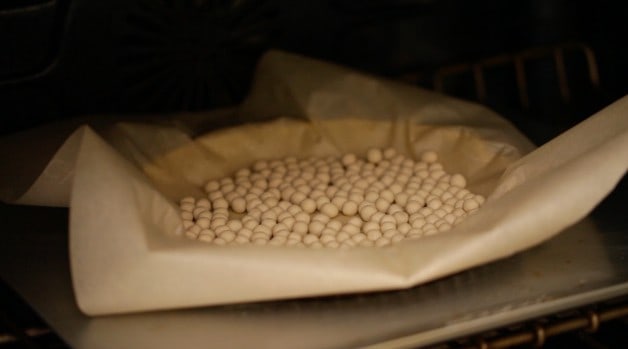 Baking beads with parchment paper over tart crust in oven