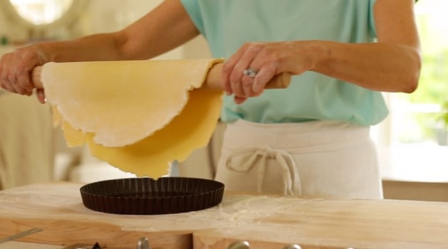 the rolled tart dough being placed in a tart pan