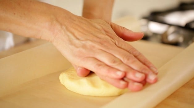 Two hands pressing dough ball into a disk for tart dough