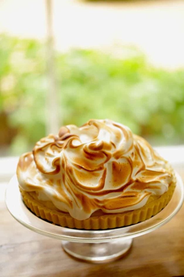 Vertical Image of a Lemon Meringue Tart on a cake stand in front of a window