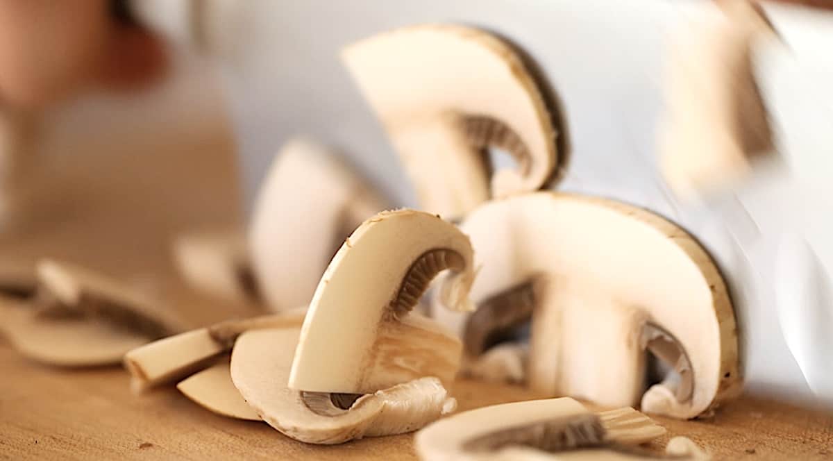 slicing mushrooms with a chef's knife on a cutting board