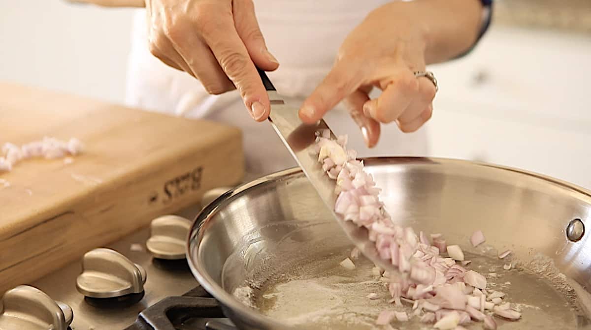a person adding minced shallots from a chef's knife into a skillet