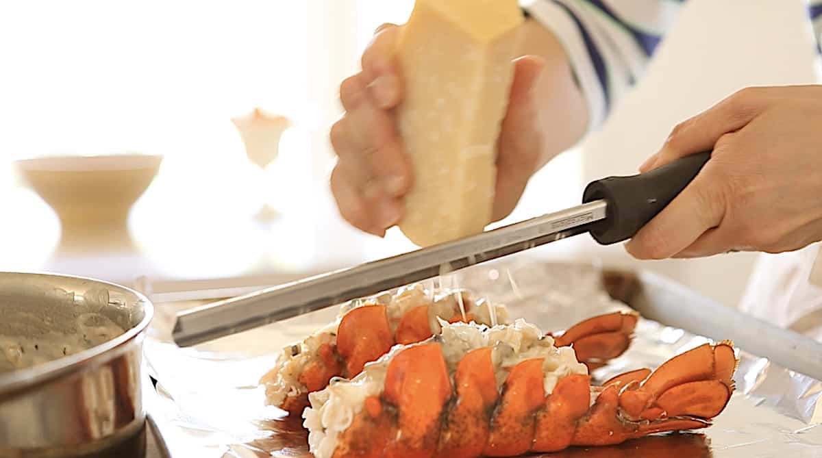 a person adding grated cheese to a freshly baked lobster thermidor