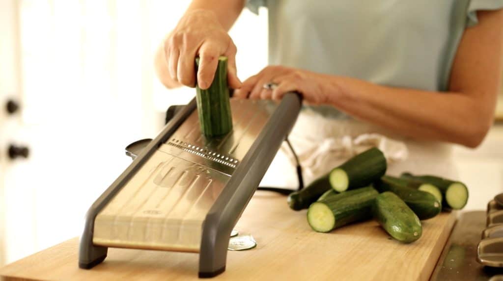 English cucumbers being sliced in a mandoline 