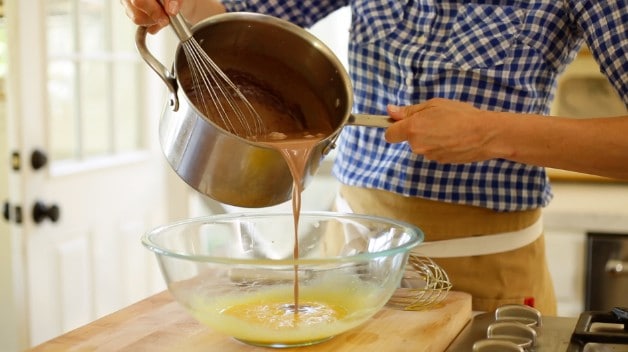 Adding chocolate mixture from a pot into the egg yolk mixture in a clear bowl