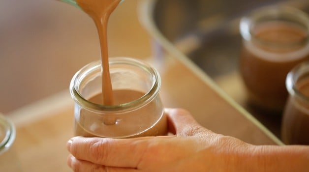 A person pouring chocolate pudding into a glass jam jar