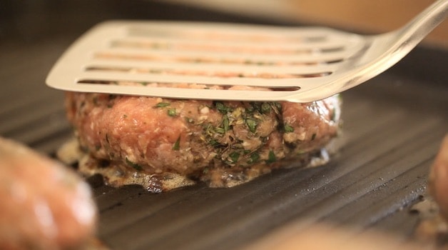 Flattening a burger on a grill with a spatula