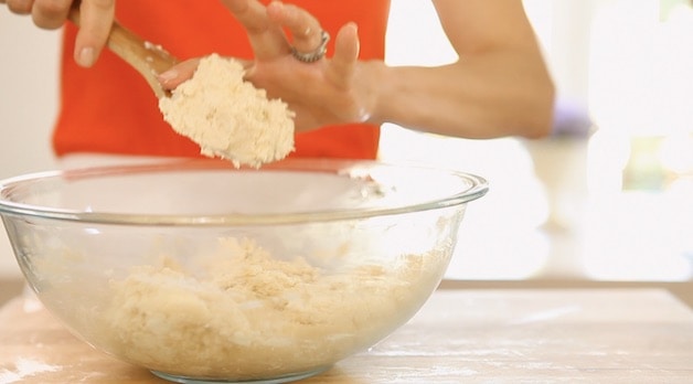 Scrapping dough off a wooden spoon into a clear bowl