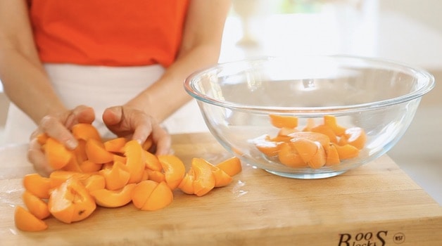 Adding sliced apricots into a large glass bowl