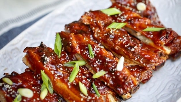 BBQ Ribs garnished with green onions and sesame seeds on white platter