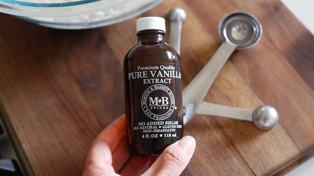 hand holding a bottle of vanilla over a cutting board with measuring spoons