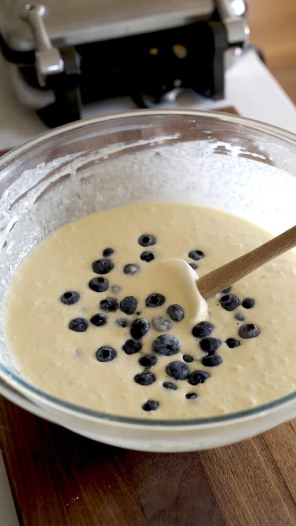 Waffle batter with blueberries and a spatula in the batter resting